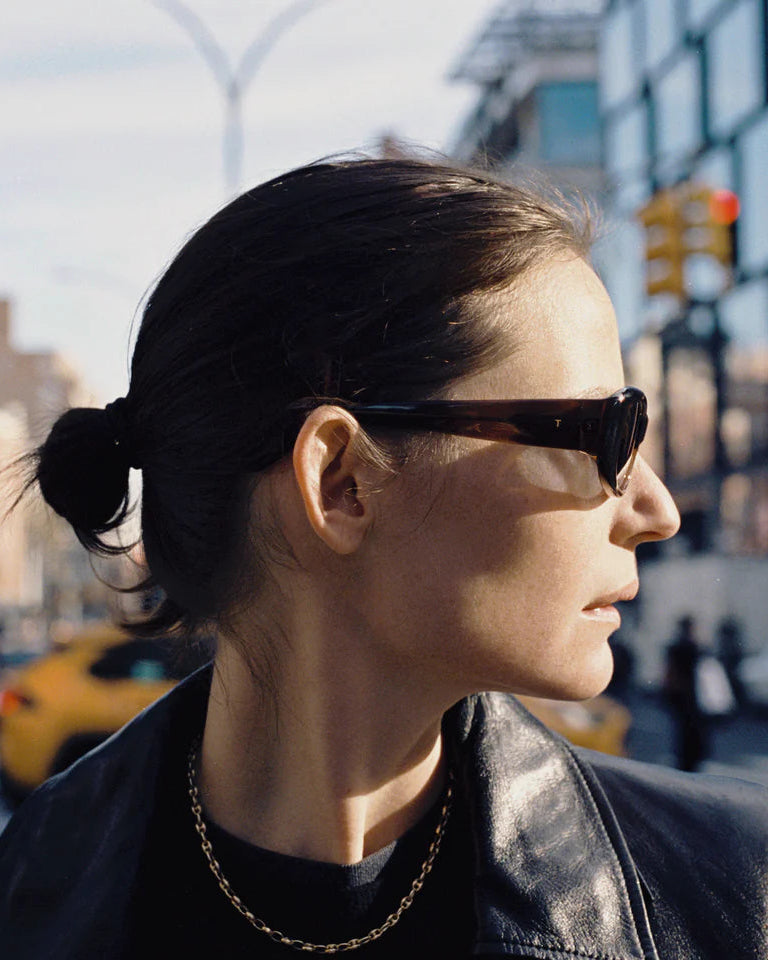 Person wearing sunglasses on a city street with buildings and traffic lights in the background