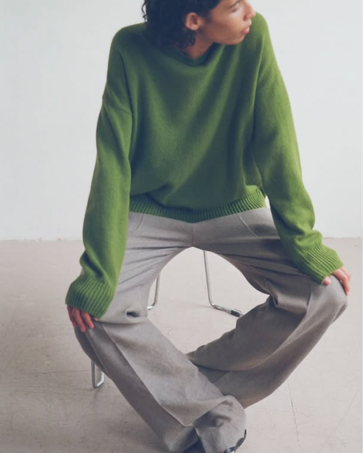 Person wearing a green sweater and gray pants sitting on a white floor.