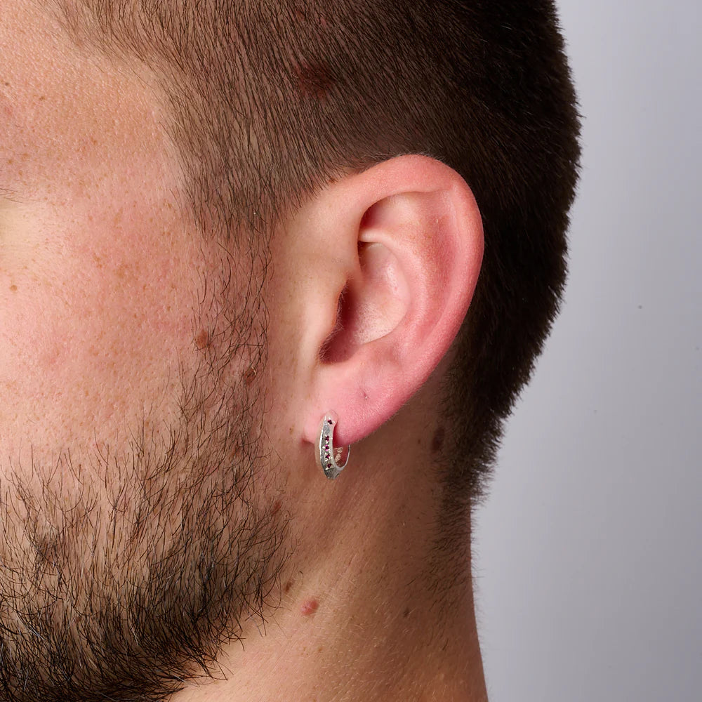 Close-up of a man's ear wearing a silver hoop earring against a neutral background