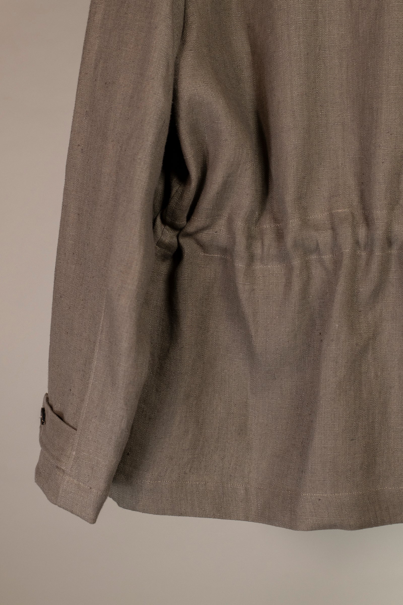 View from back looking at bottom and left sleeve of Wanze men's natural linen field jacket in brown